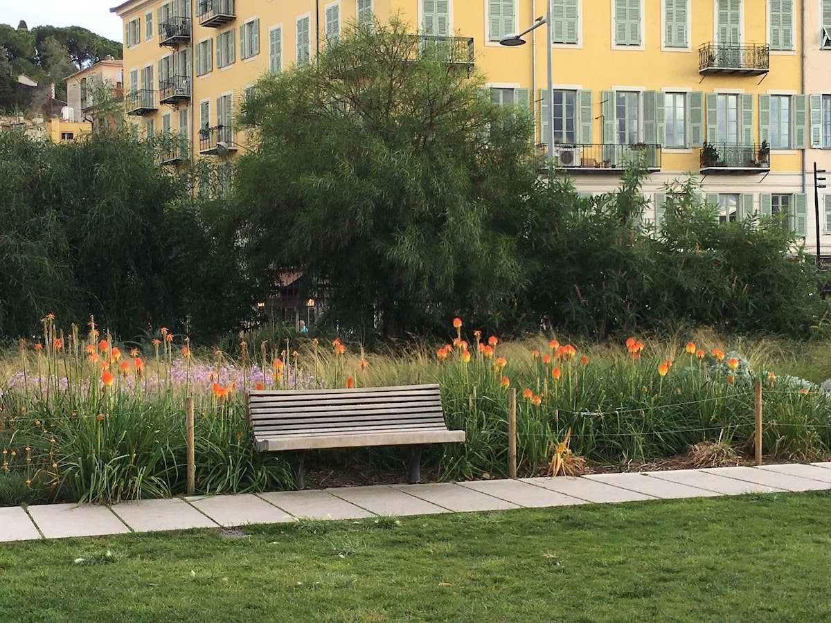 Promenade du Paillon, einsame Parkbank mit Blumen dahinter.