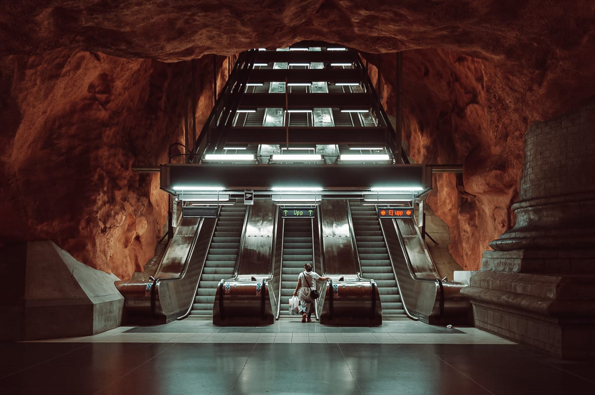 Tunnelbana-Haltestelle Rådhuset, Stockholm - 3 Rolltreppen mit einer Frau in der Mitte, griechische Säule rechts