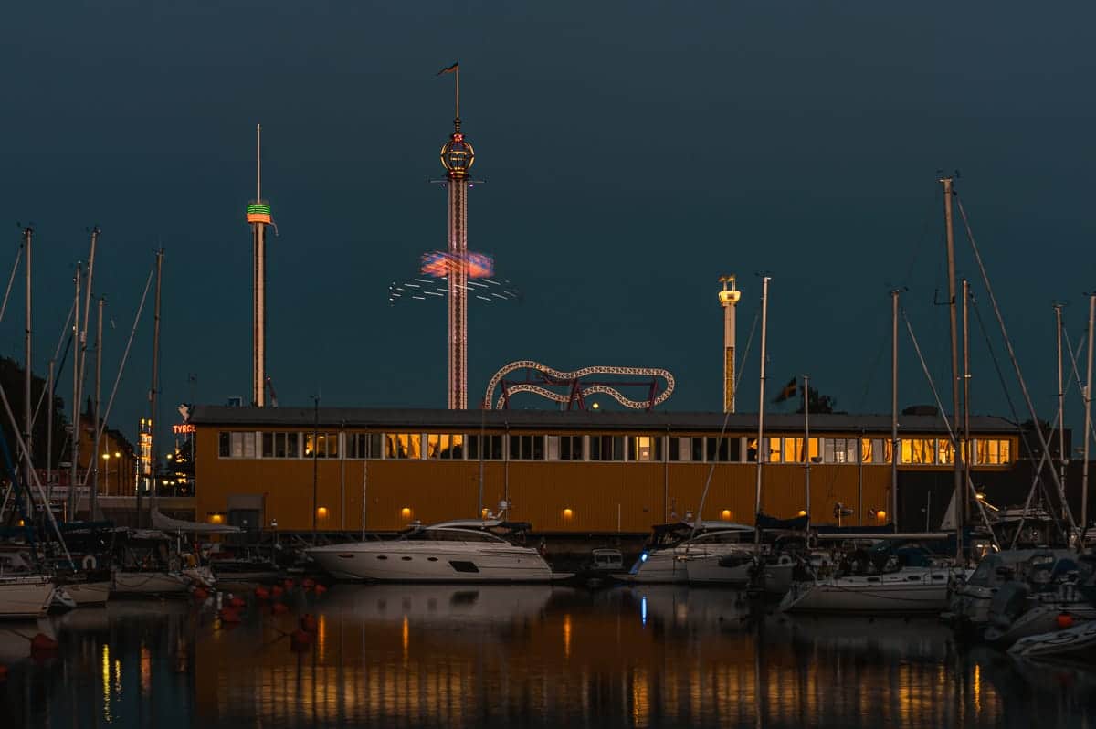 Kleiner Yachthafen im Vordergrund mit Gröna Lund im Hintergrund, beleuchtet, zur blauen Stunde.