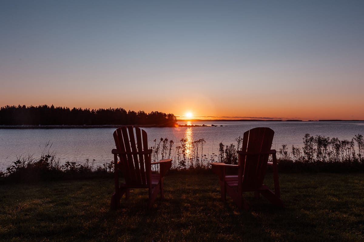East Shores Nova Scotia, Sonnenaufgang über dem Wasser, direkt an einer Insel, zwei typisch kanadische Deckchairs im Vordergrund.