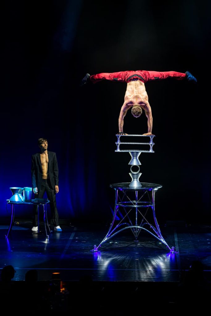 Maxim Kriger mit seiner Rola Rola Akrobatik - er macht einen Handstand mit einem Spagat der Beine in der Luft auf drei Rollen und drei Brettern.