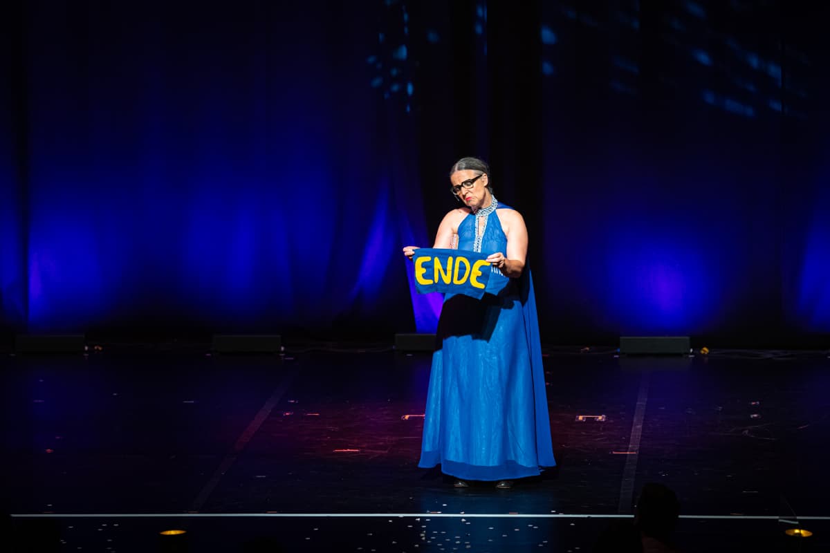 Alles hat ein Ende, auch "Wild Boys". Rosemie hält in einem langen blauen Abendkleid ein Stoff mit dem Wort "Ende" hoch.