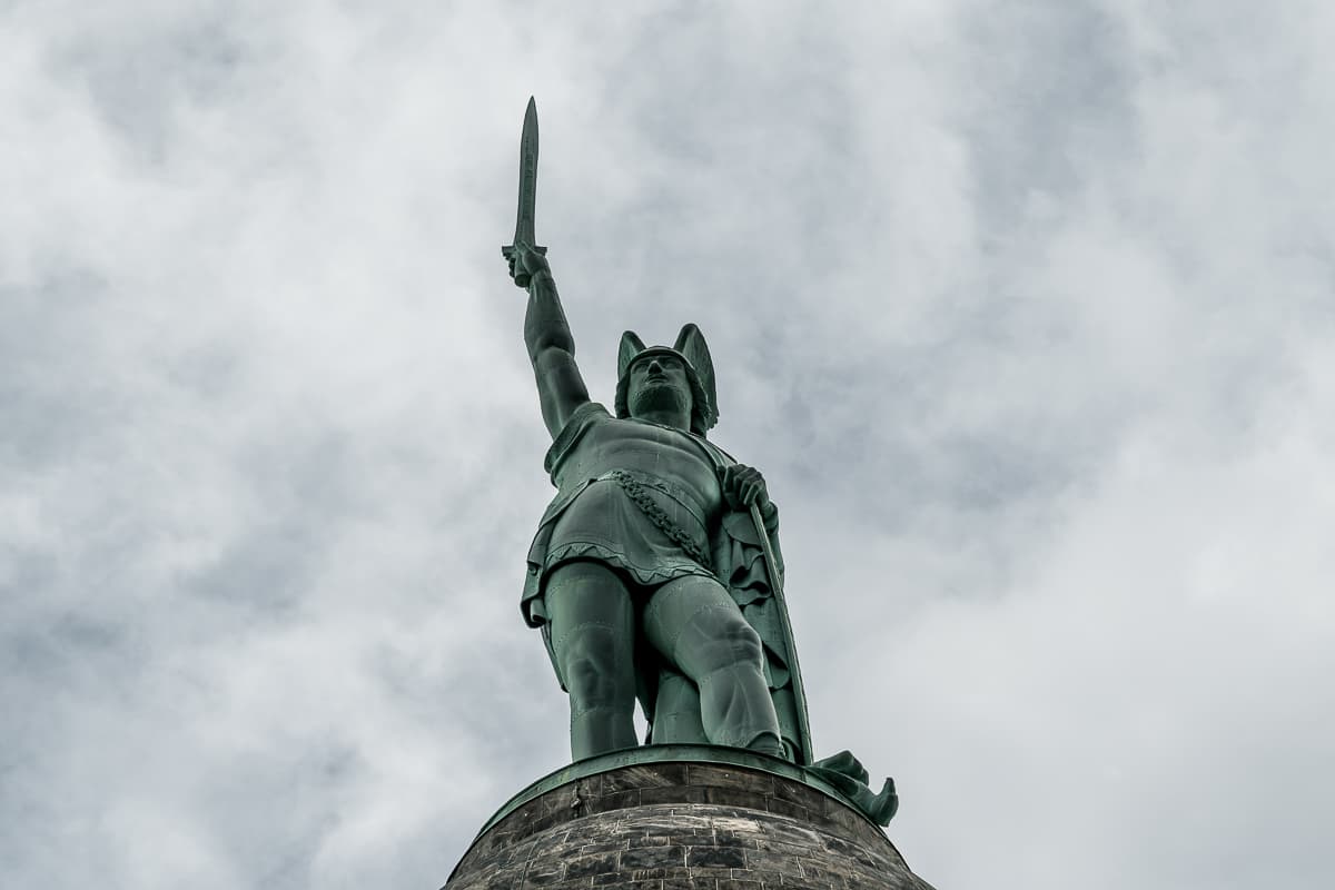 Hermannsdenkmal in Detmold - Nahaufnahme von unten des Hermanns mit dem Schwert in der rechten Hand, das er zum Himmel reckt, links auf das Schild stützend, auf einen Adler tretend.