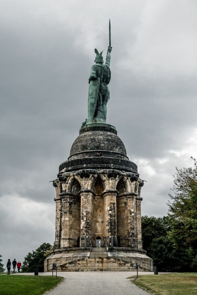 Weg zum Hermannsdenkmal - Ansicht von hinten mit Aufgang zum Denkmal, Weg zentral darauf zuführend, dahinter dunkle Wolken.