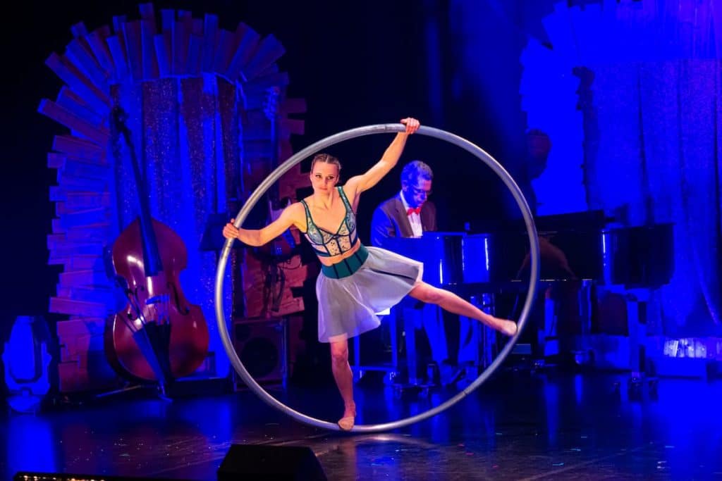 Cléa am Cyr Wheel, ein großer Metallring, den sie wie ein Rhönrad nutzt, also auf und in ihm rumwirbelt. Musiker der Begleitband im Hintergrund. 