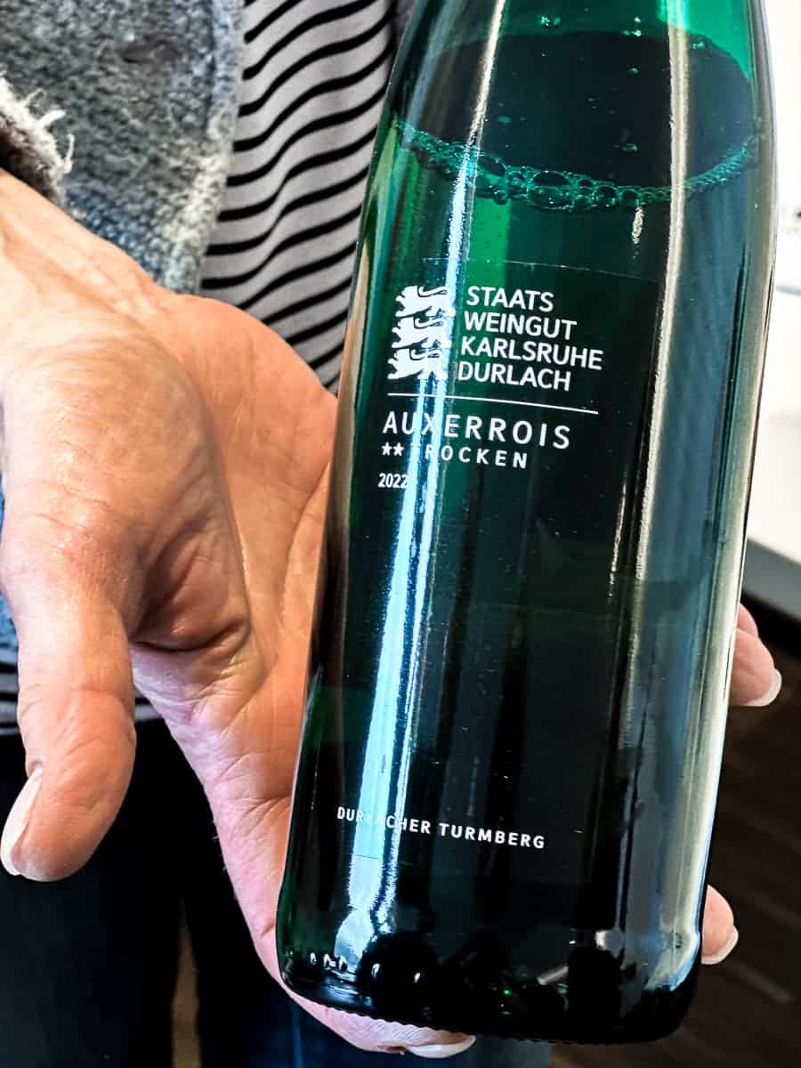 Eine Hand hält eine angfangene Flasche Auxerrois des Staatsweingutes Karlsruhe-Durlach in die Kamera.