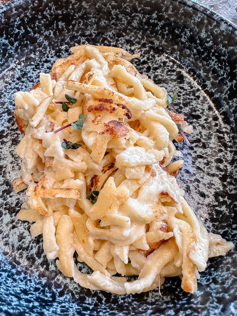 Käsespätzle auf einem dunklen marmorierten Teller, liebevoll angerichtet - Gasthaus Gutenberg, Karlsruhe Weststadt.