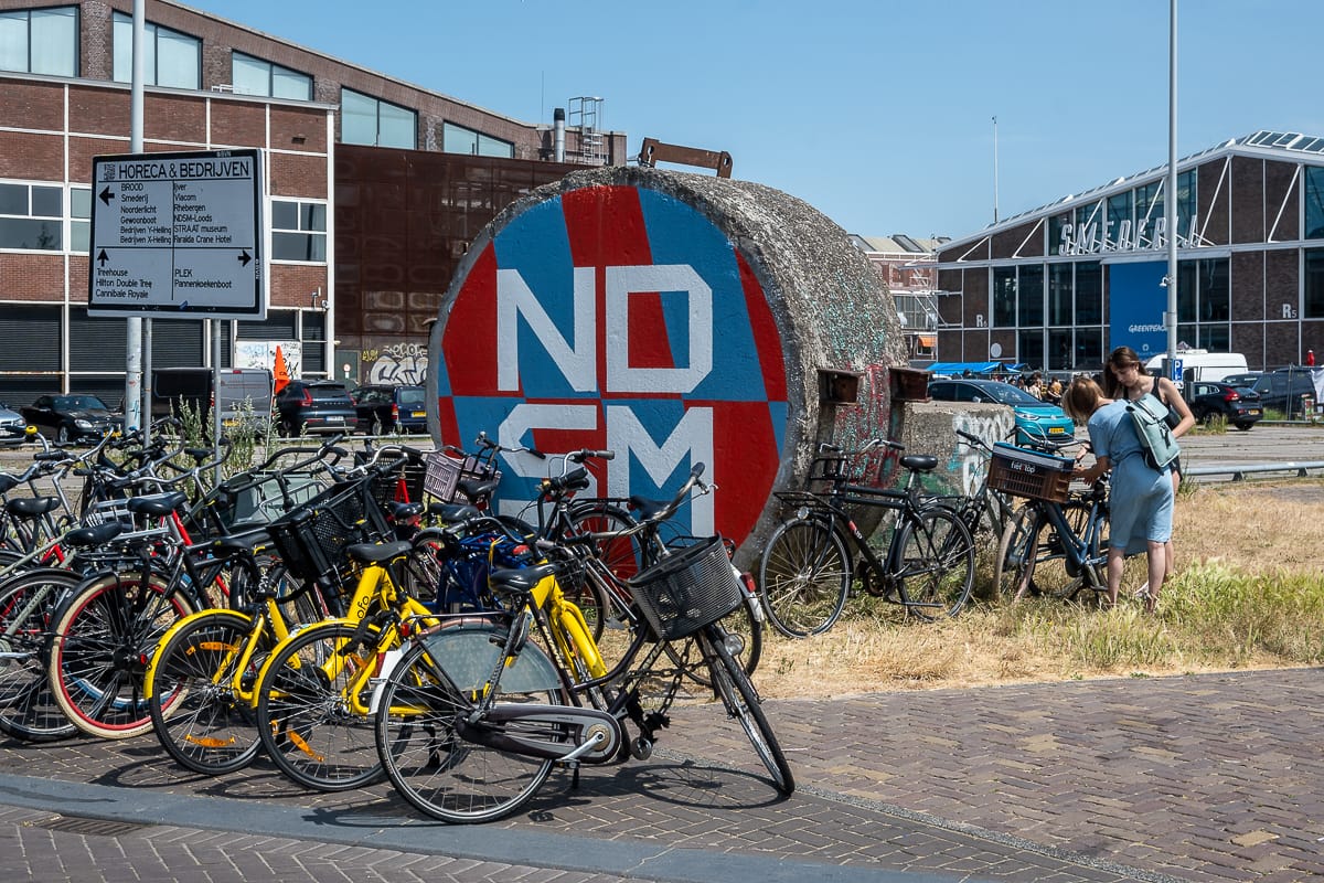 Fahrräder stehen vor einem Kunstwerk, dass NDSM aufgesprüht hat, vor alten Werfthallen in Amsterdam-Noord.