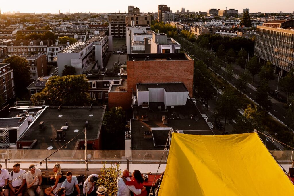 Blick von oben auf die Dachterrasse des Restaurant Canvas, Volkshotel Amsterdam mit Blick auf Amsterdam bei Sonnenuntergang.