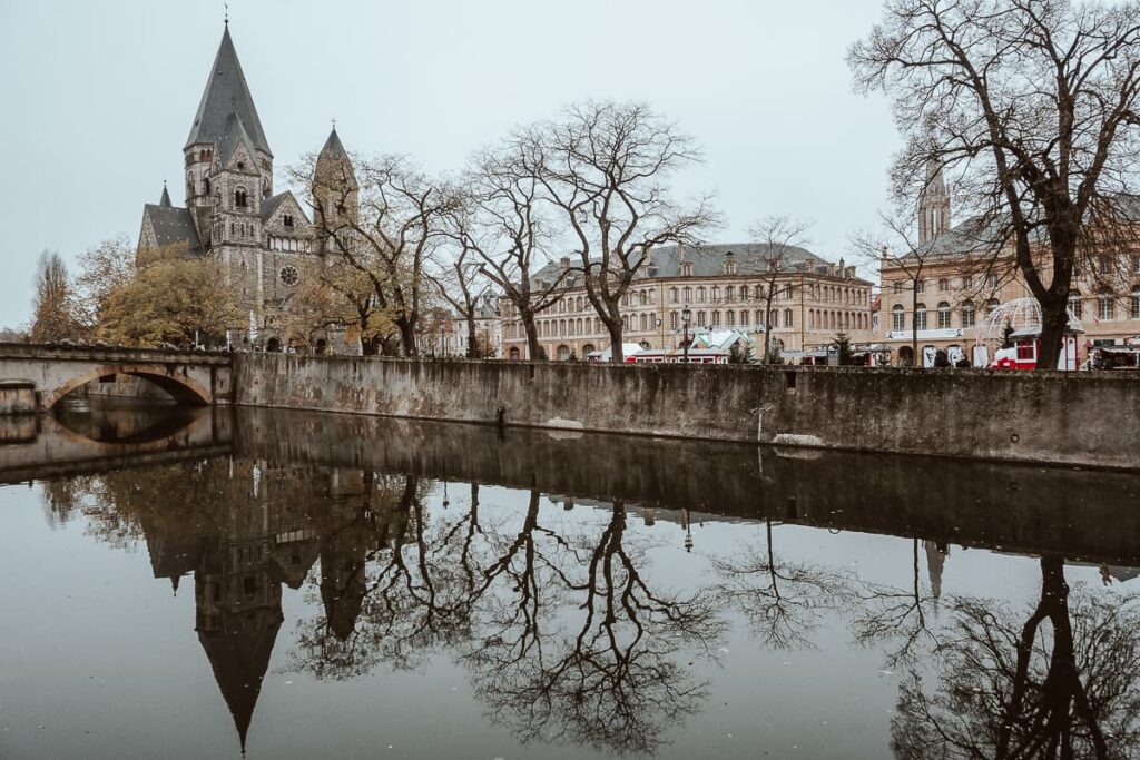 Weihnachtsmarkt Metz auf dem Place de la Comédie und Kirche Temple Neuf von einer Brücke gesehen, Spiegelung im Wasser.