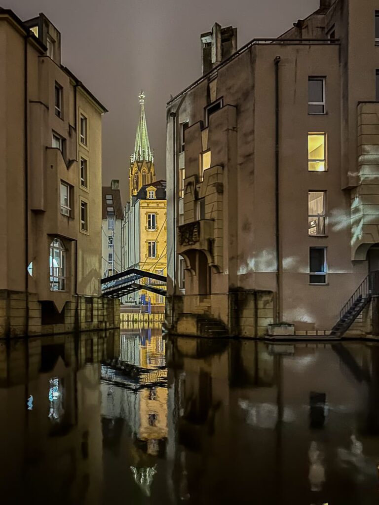 Blick zwischen von mit Schneeflocken beleuchtete Häusern auf den Turm der ehemaligen Garnisonskirche, Metz.