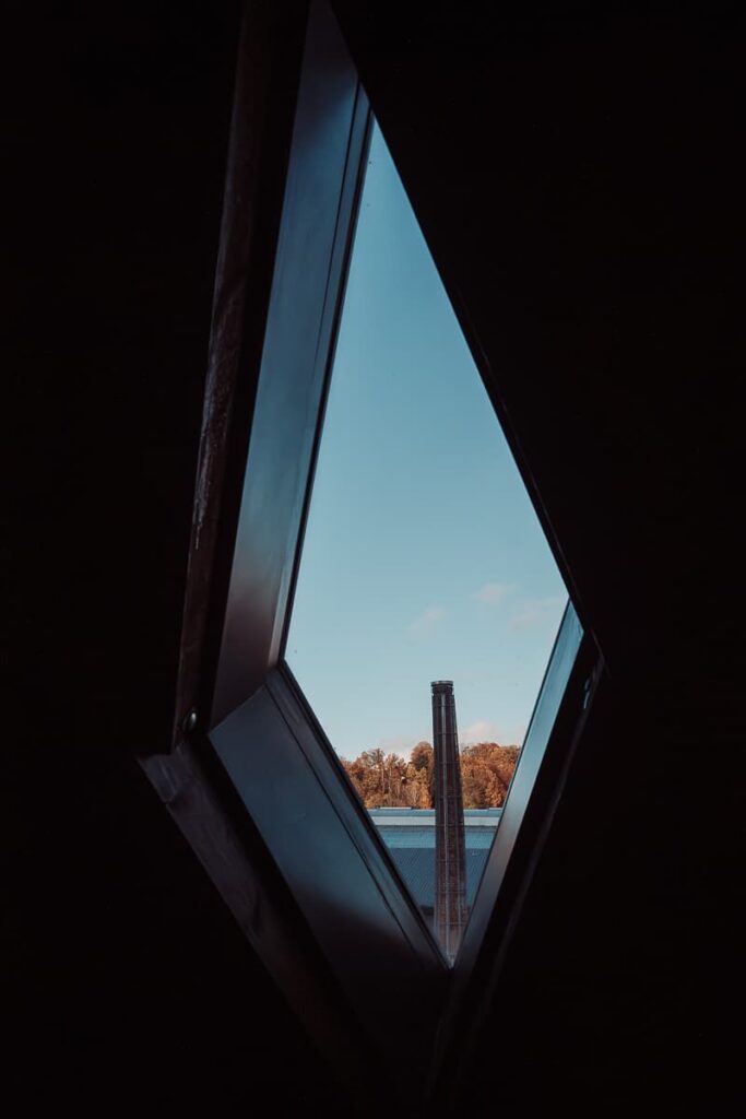 Blick auf den windschiefen Schornstein in Meisenthal aus einem rautenförmigen Fenster des Glasmuseum heraus.
