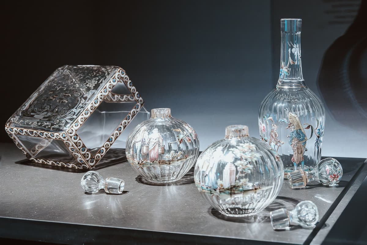 Bemahlte Glaswaren, 2 kleine runde Vase, eine quadratische Box und eine Flasche mit Glasverschluss, reichlich verziert, bäuerliche Motive, im Glasmuseum Meisenthal.