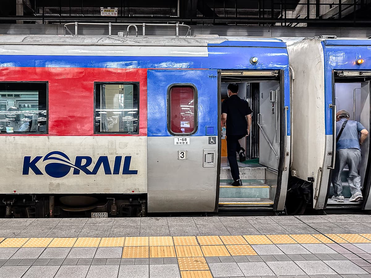 Wagon eines KTX am Gleis der Yongsan Station mit offener Tür, eine Person steigt die Treppenstufen im Wagon hoch, rechts daneben ein weiterer Wagon mit geöffneter Tür und einsteigendem Gast.