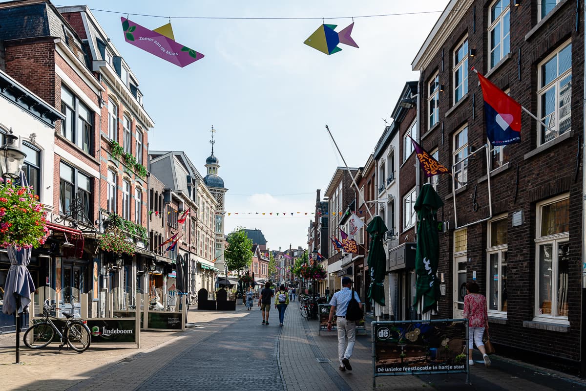 Straße "Parade" in Venlo, eine Einkaufsstraße, geschmückt mit Fahnen und Blumenkästen, Menschen flanieren an den Geschäften entlang.