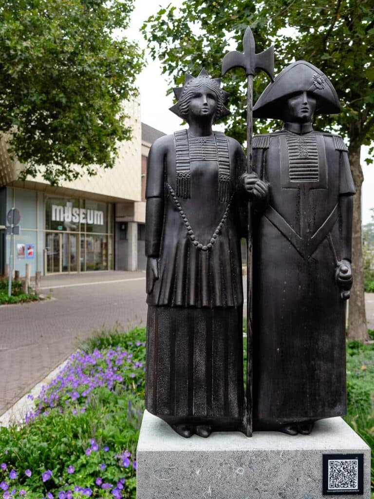 Statue mit historischen Figuren in traditioneller Kleidung am Museum van Bommel van Dam in Venlo. Unten rechts ein QR-Code.