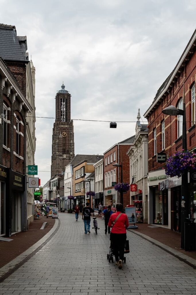Langstraat mit Blick auf die Martinuskerk in Weert. Straße macht leichten Linksknick. Einkaufende Personen schlendern die Streaße entlang.