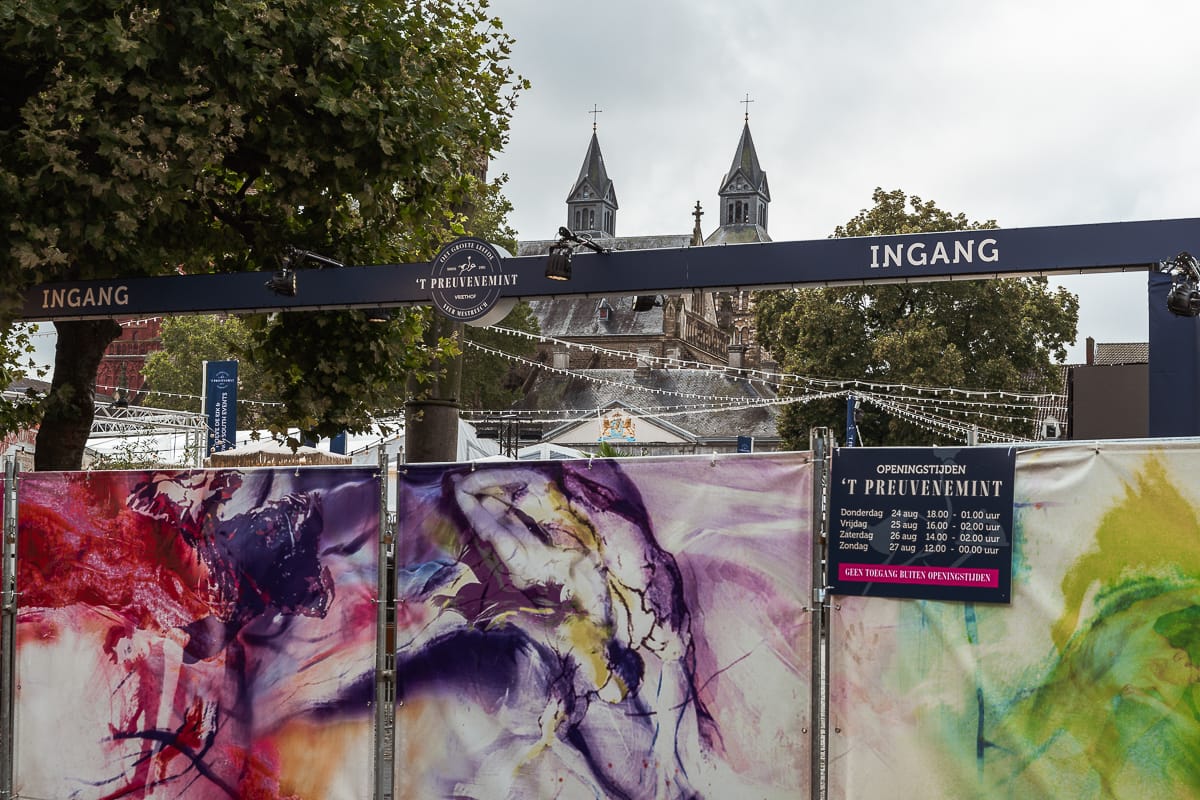 Eingang 't Preuvenemint auf dem Vrijthof, noch vor Eröffnung abgesperrt mich blickdichten Absperrungen, einem Balkan darüber mit der Aufschrift "Ingang" und einem Schild mit den Öffnungszeiten. 
