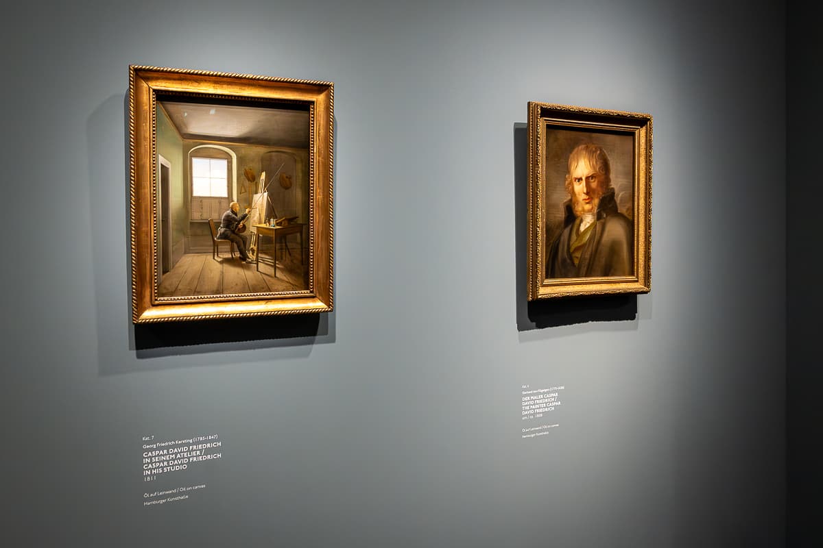 Zwei Gemälde von unerschiedlichen Malern von Caspar David Friedrich, Kunsthalle Hamburg. Links zeigt den Maler an einer Staffelei sitzend, in einem Atelier. Das linke ist ein klassisches Portrait mit Backenbart und hochgestelltem Mantelkragen.