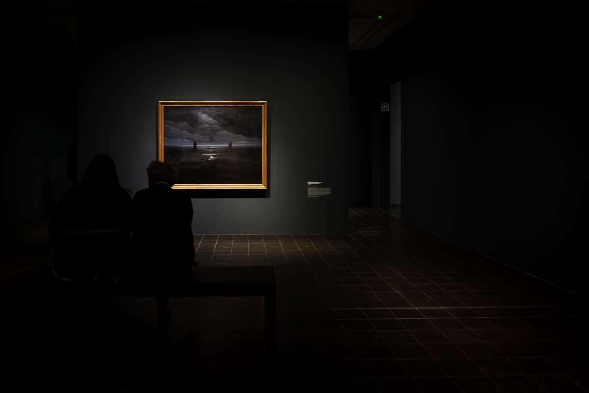 Sitzende Person im Halbdunkel vor dem großen, letzten Bild von Caspar David Friedrich in der Kunsthalle Hamburg: Meeresufer im Mondschein, 1835/36, Öl auf Leinwand, Hamburger Kunsthalle. 