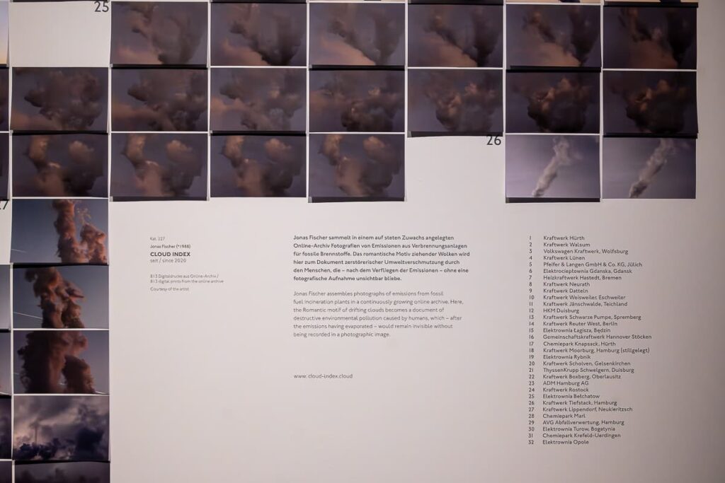 Collage von vielen Fotos mit Industrieabgasen, Wolken, Dazu Text, von welchen Kraftwerken die Bilder stammen und Begleittext darunter. Jonas Fischer, CLOUD INDEX, seit 2020, wachsendes Online-Archiv, das Wolkenbilder von Verbrennungsanlagen für fossile Brennstoffe sammelt und präsentiert, Courtesy of the artist.