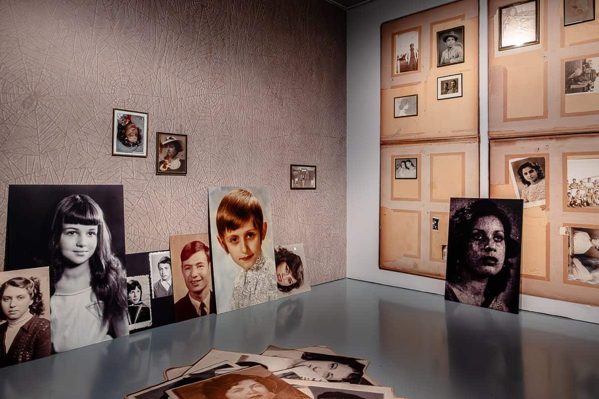 Blick in den Raum mit übergroßen Pass- und Familienfotos sowie Fotoalben, die an der Wand angebracht sind oder an einer anderen Wand gelehnt oder auf dem Boden liegen. Projekt von Erik Kessels, "Album Beauty", 2012.
