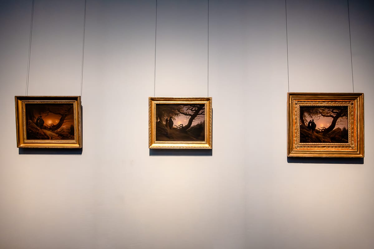 Drei ähnliche Bilder nebeneiner, eher kleinformatig, Variationen von "Zwei Männer in Betrachtung des Mondes" (linkes Bild, 1819/20), Männer eher links, einer hat Arm auf Schulter des anderen, auf einer Anhöhe, ein knorriger Baum daneben, Mond eher mittig. Bild in der Mitte zeigt die Variation "Mann und Frau in Betrachtung des Mondes" (1824), etwas heller als das vorherige Bild, rechts auch helleres Bild, wieder zwei Männer (1830-35), Caspar David Friedrich, Alte Nationalgalerie.