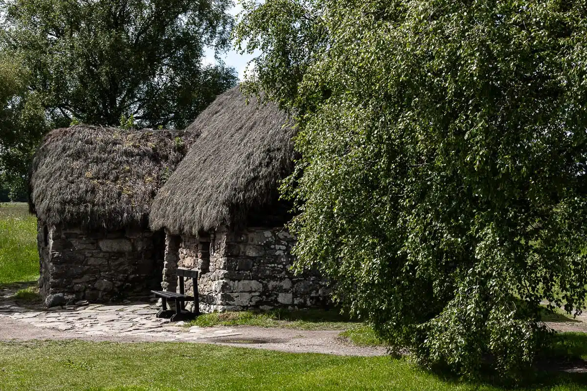 Leanach Cottage, ein kleines Häuschen, reetgedeckt, grobe Steine, eine Bank davor, neben der Eingangstür.