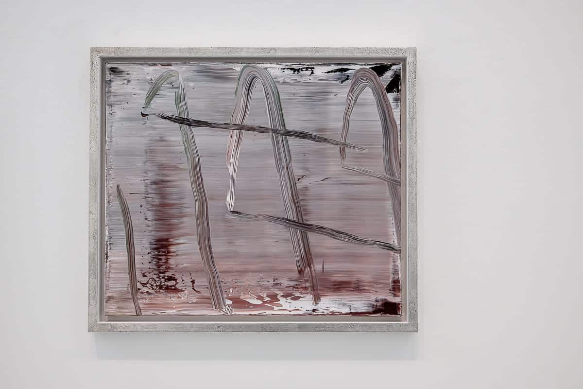 Abstraktes Gemälde von Gerhard Richter mit einer Mischung aus horizontalen Pinselstrichen in Grau und Braun, durchzogen von gebogenen und geraden vertikalen Linien in dunkleren Farbtönen. Das Werk ist in einem einfachen, strukturierten Rahmen vor einer schlichten weißen Wand angebracht.