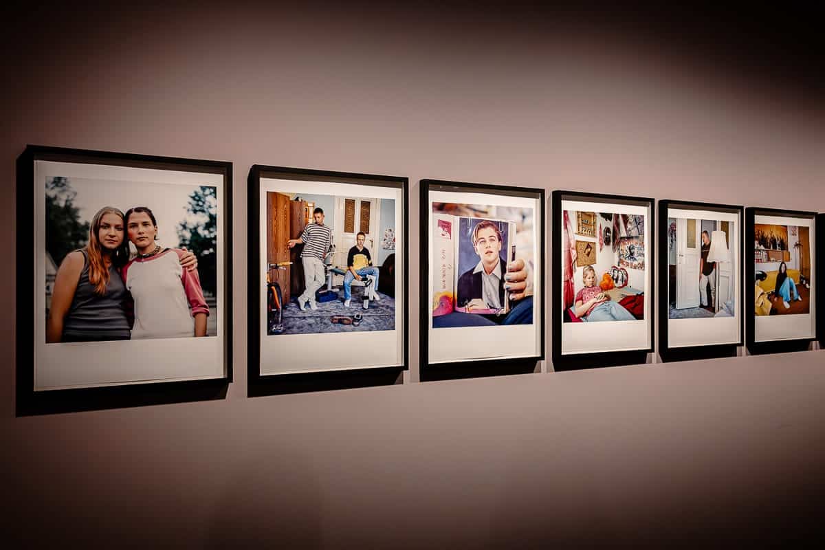 Eine Serie von sechs gerahmten Fotografien von Ostkreuz-Fotografin Anne Schönharting an einer Galeriewand im C/O Berlin. Jeder Rahmen enthält ein Foto, das Menschen in verschiedenen Innenräumen zeigt und persönliche oder intime Momente suggeriert. Die Bilder sind gleichmäßig verteilt und sanft beleuchtet, wodurch ihre Farben und Details vor der neutralen Wand hervorgehoben werden.