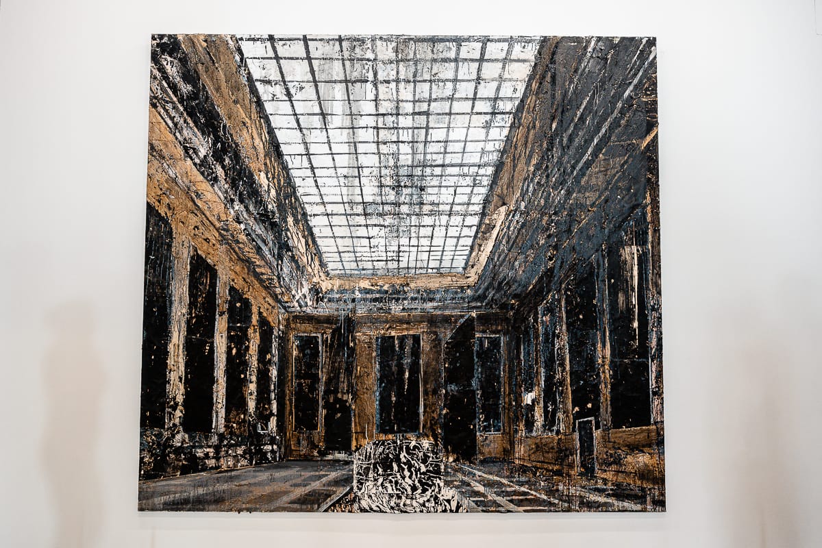 Ein großes, strukturiertes Gemälde eines kunstvollen, verfallenen Raumes mit hohen Säulen, hohen Fenstern und einer Glasdecke. Die Farben sind überwiegend dunkelbraun, schwarz und grau, wobei die grobe Pinselführung von Anselm Kiefer einen verwitterten, gealterten Look erzeugt. Auf beiden Seiten erscheinen zwei verschwommene Silhouetten.