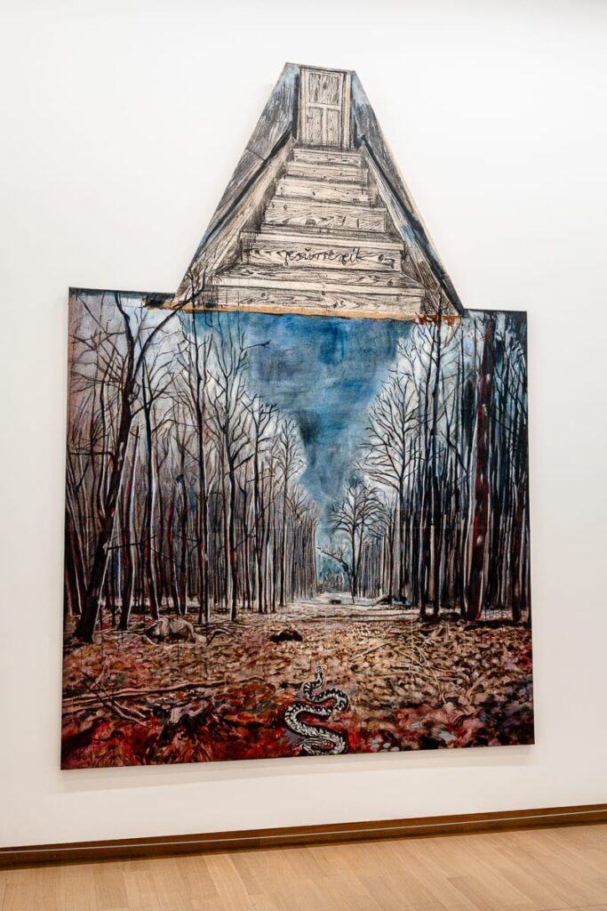 Ein Gemälde von Anselm Kiefer zeigt einen blattlosen Wald mit wolkenblauem Himmel, kahlen Bäumen und einer Schlange, die zwischen gefallenen Blättern hindurchgleitet. Über der Szene ragt eine dreieckige, dachbodenartige Struktur mit Holztreppe und geschlossener Tür hervor und verbindet surreale Elemente mit Realismus.