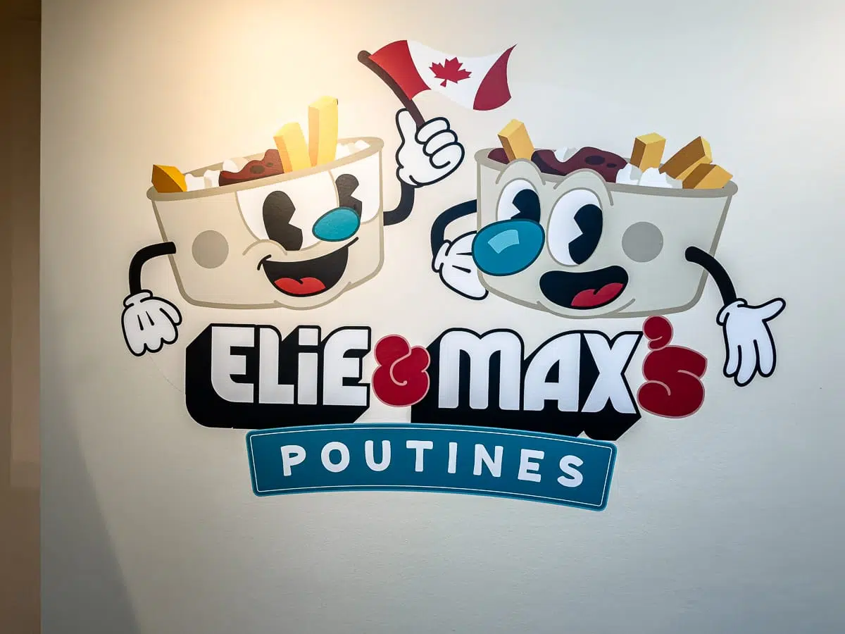 Cartoon-Poutine-Schalen mit lächelnden Gesichtern schwenken eine kanadische Flagge über dem Text "Elie & Max's Poutines" auf einem Wandschild, das Elie & Max's Poutines mit klassischen Pommes frites, Cheese Curds und reichhaltiger Soße feiert.